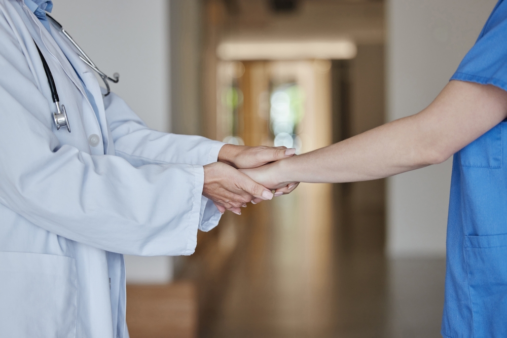 Doctor holding another healthcare professional’s hands in a hospital hallway, symbolizing accountability and patient care.