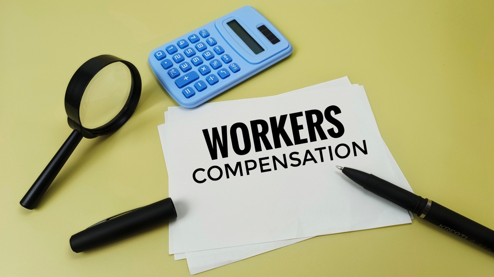 A document labeled workers compensation beside a magnifying glass and calculator, representing the process of filing a claim in Montana.