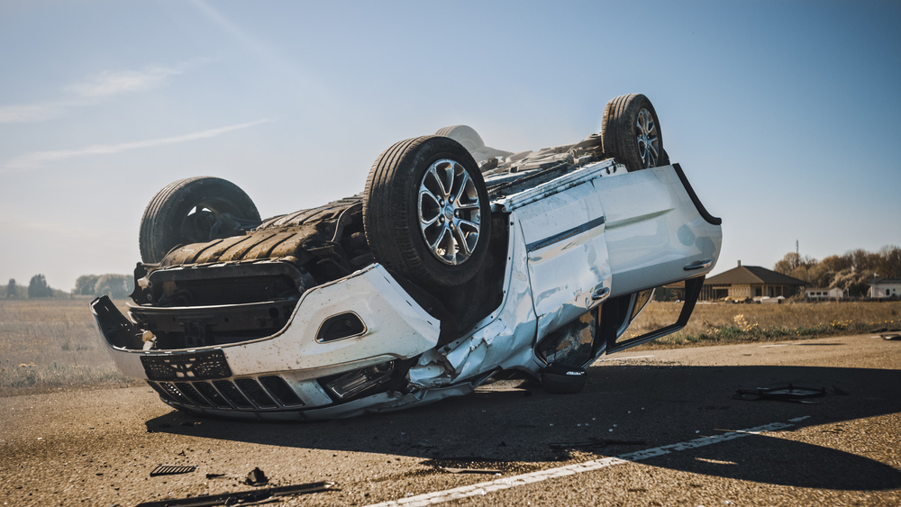 An overturned white car on a rural road under clear skies, symbolizing the tragic consequences of a fatal car crash in Montana