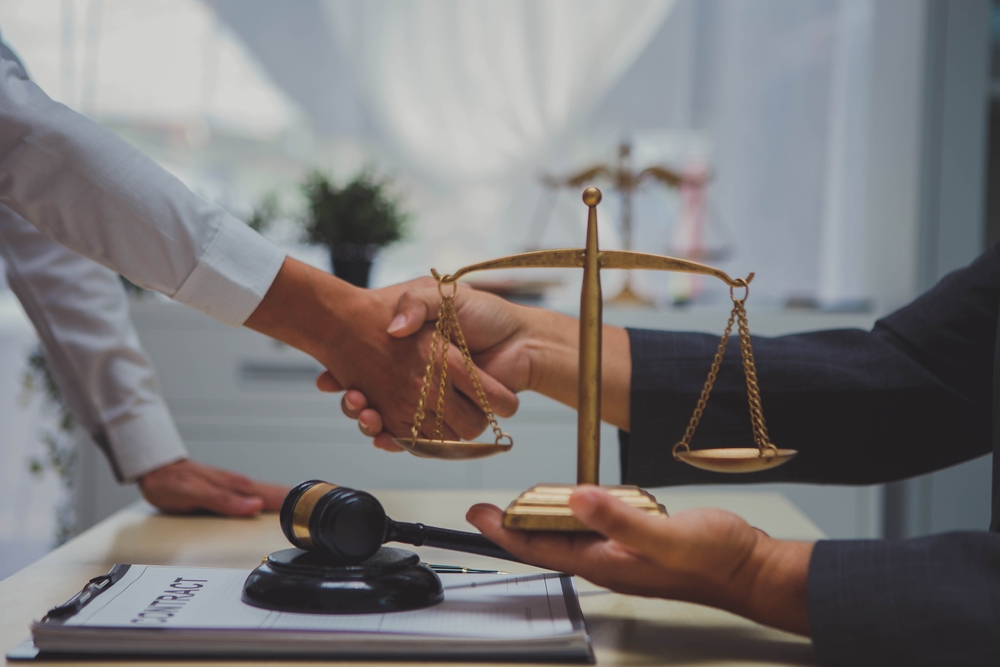 A lawyer and client shaking hands beside a justice scale and gavel, symbolizing legal assistance with workers’ compensation claims in Montana.