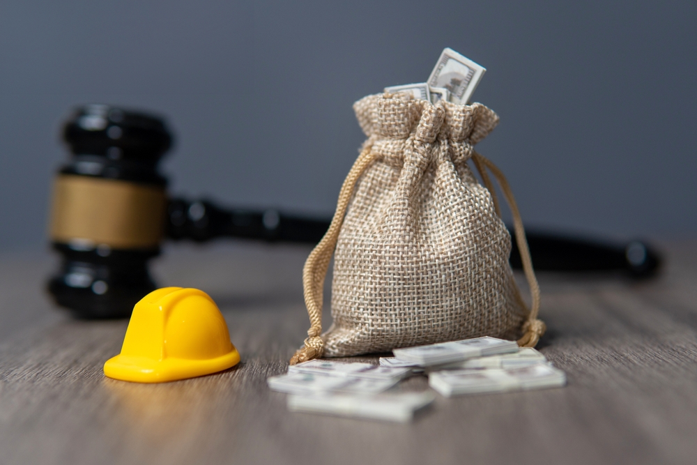 A small yellow hard hat, a money bag, and a gavel symbolizing workers’ compensation benefits under Montana law.